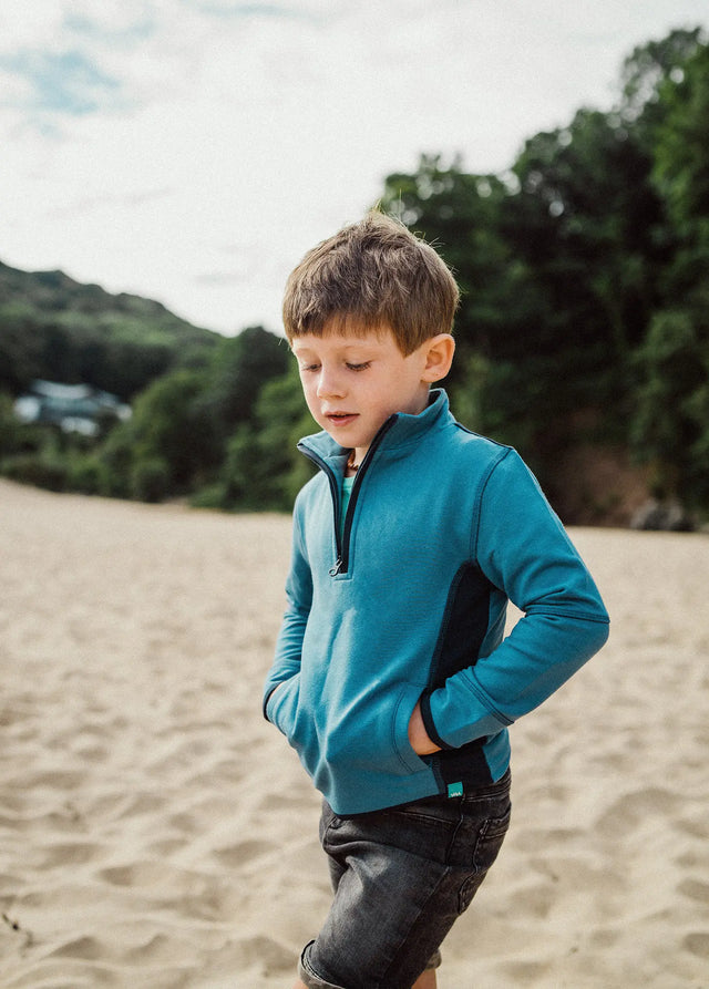 Boy walking on the beach wearing the Jellymud Kids' Ridge Sweatshirt in blue.