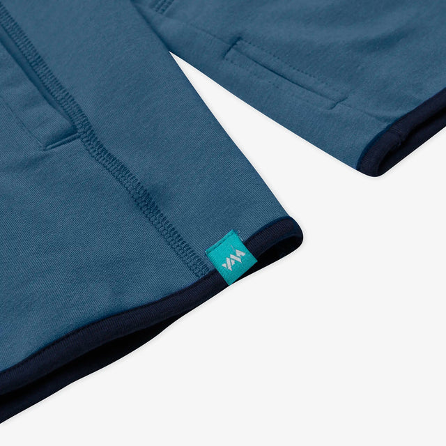 A close up view of the Jellymud Men's Peak Quarter Zip Sweatshirt in blue showing the signature embroidered hem tag in aqua.
