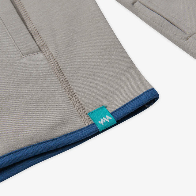 A close up view of the Jellymud Men's Peak Quarter Zip Sweatshirt in grey flint showing the signature embroidered hem tag in aqua.